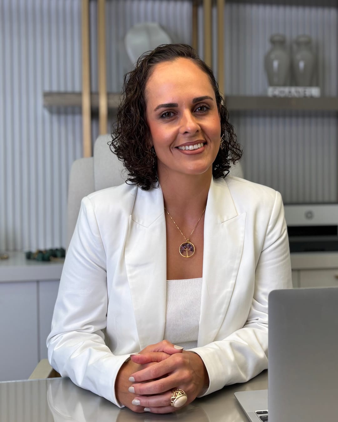Francine Sinnott sorrindo, de blazer branco, sentada à mesa com as mãos entrelaçadas.